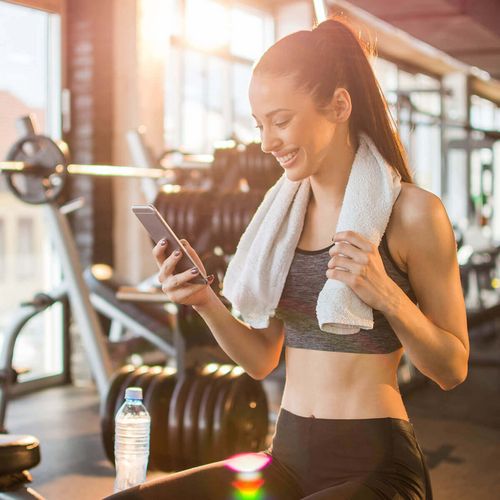 Junge Dame lächelnd am Handy im Fitnessstudio in Haslach