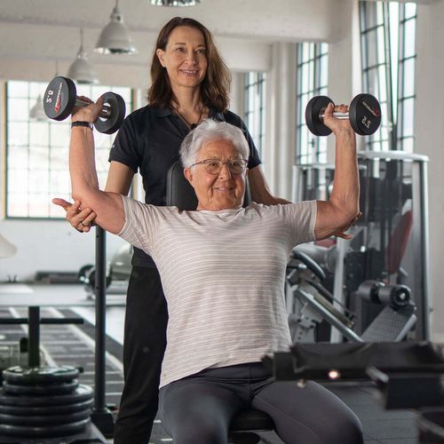 Ältere Dame mit einer Trainerin bei einer Kraftübung mit Hanteln im Fitnessstudio in Haslach