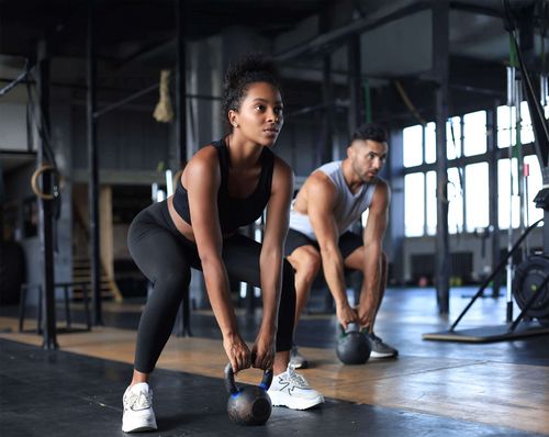 Zwei junge Erwachsene bei einer Kraftübung mit Kettle Balls im Fitnessstudio in Haslach