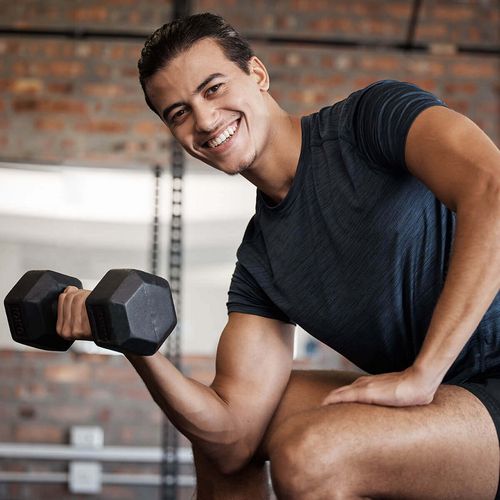 Junger Mann lächelnd beim Krafttraining mit Freihanteln im Fitnessstudio in Haslach