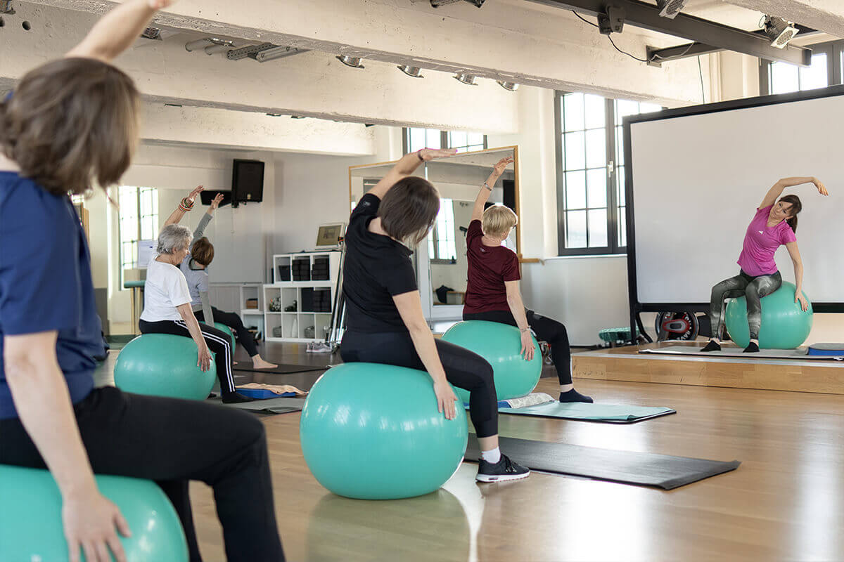 Mehrere Personen bei einem Kurs sitzend auf Medizinbällen im Fitnessstudio in Haslach